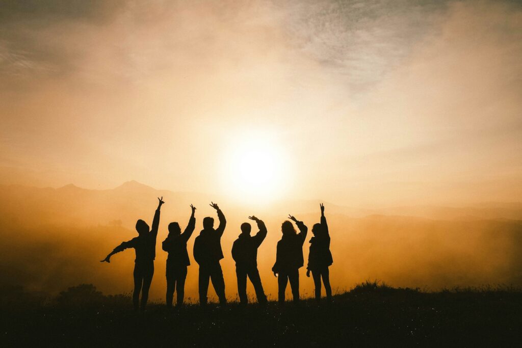 six silhouetted figures holding peace signs up in a rising sun